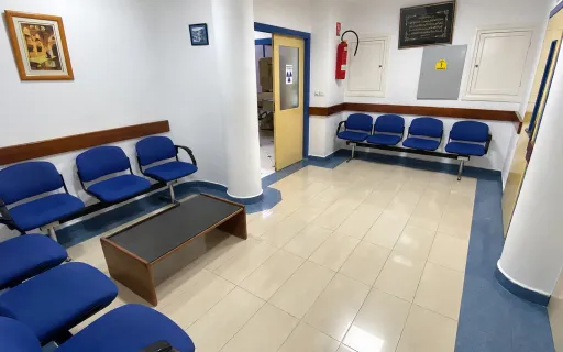 Clinic waiting room with blue seating and an open door to an examination room.